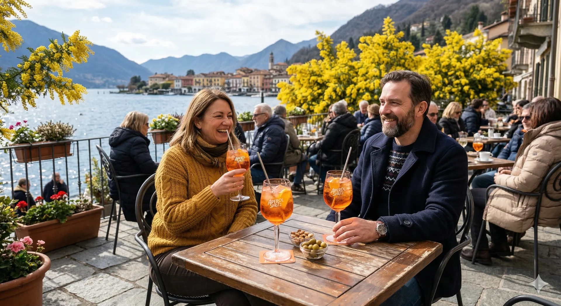 An Aperol Spritz on a lakefront terrace with golden mimosa blossoms in the background