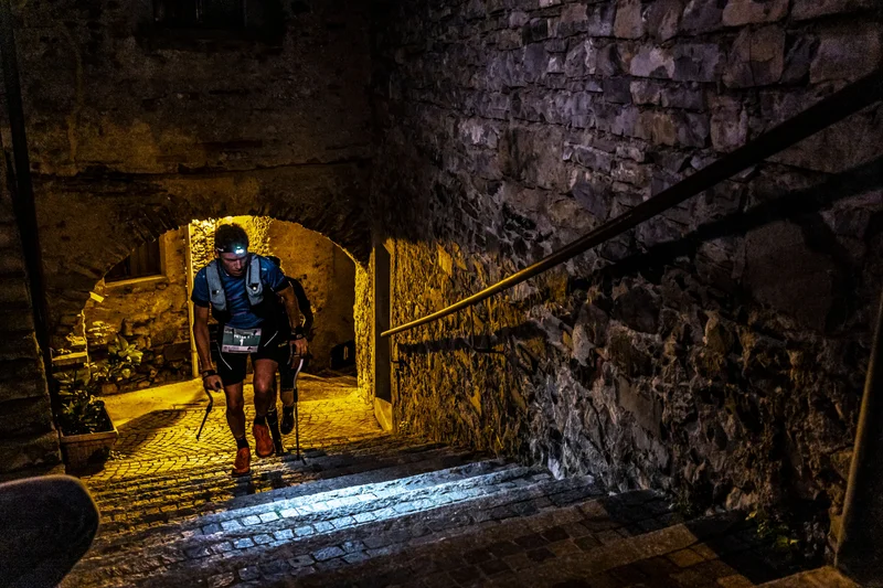 Ultra trail runner navigating stone village steps by headlamp during the UTLAC night stage